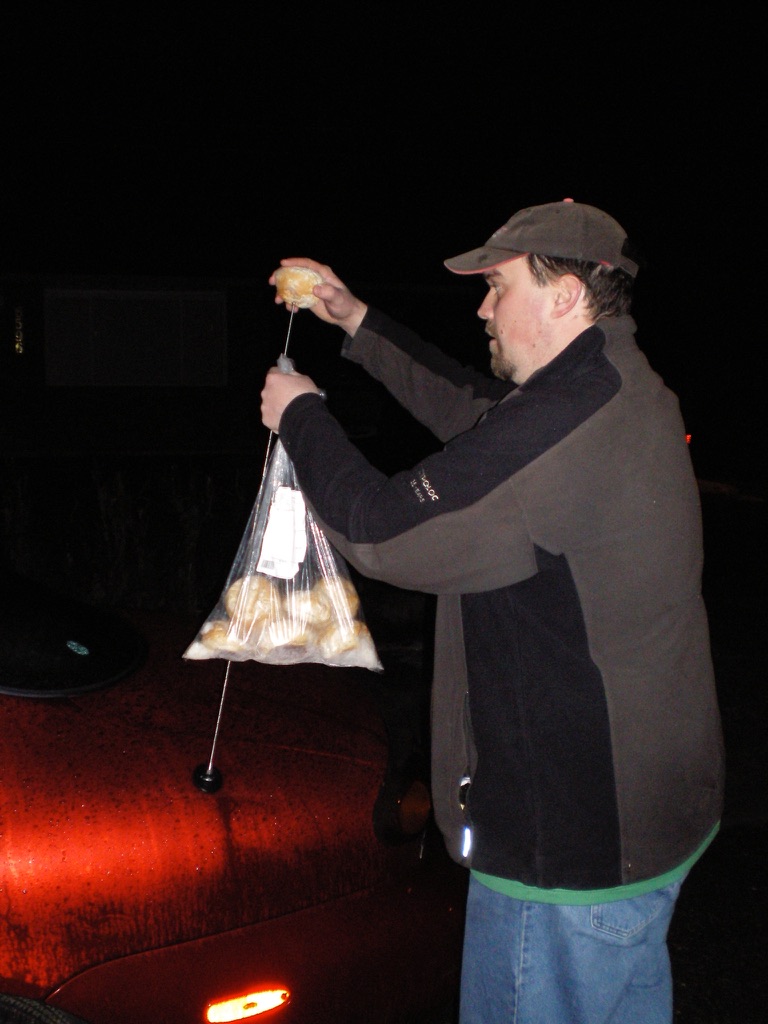 Placing a bun on a red car's antenna at night.