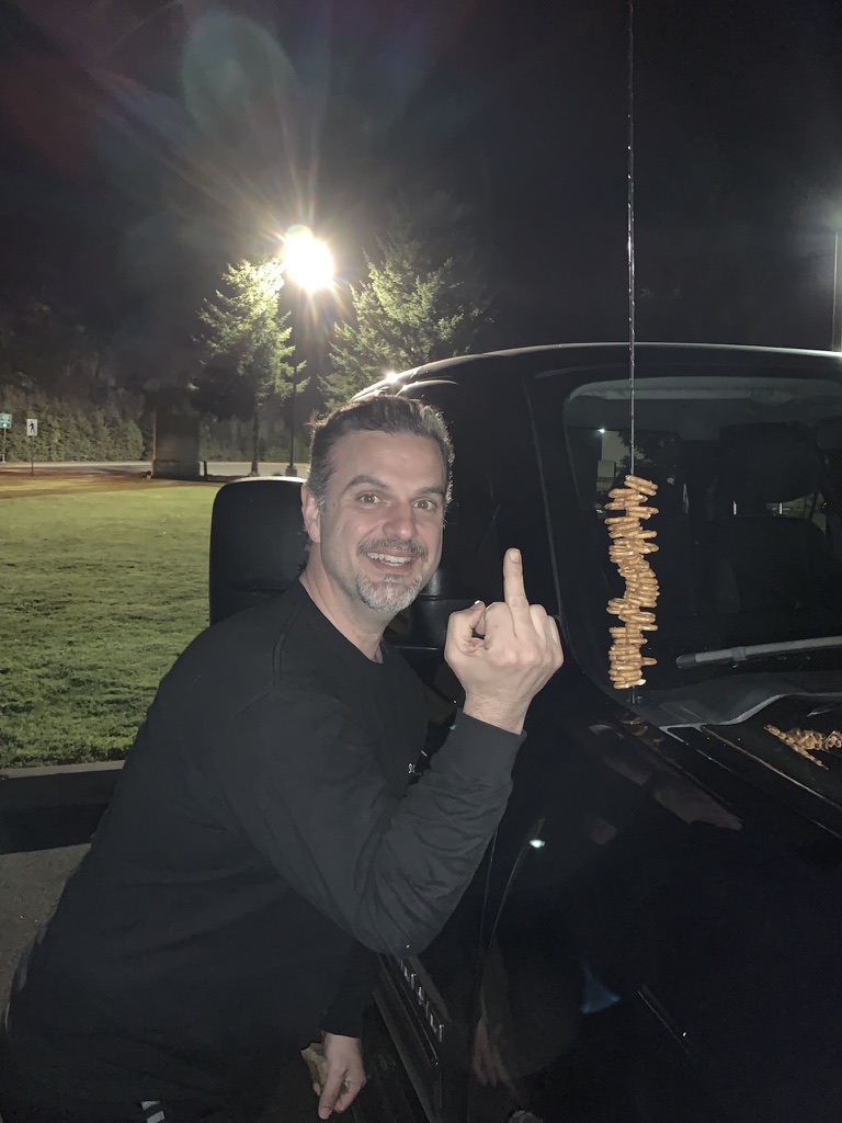 Posing beside a car antenna stacked with ring-shaped snacks.